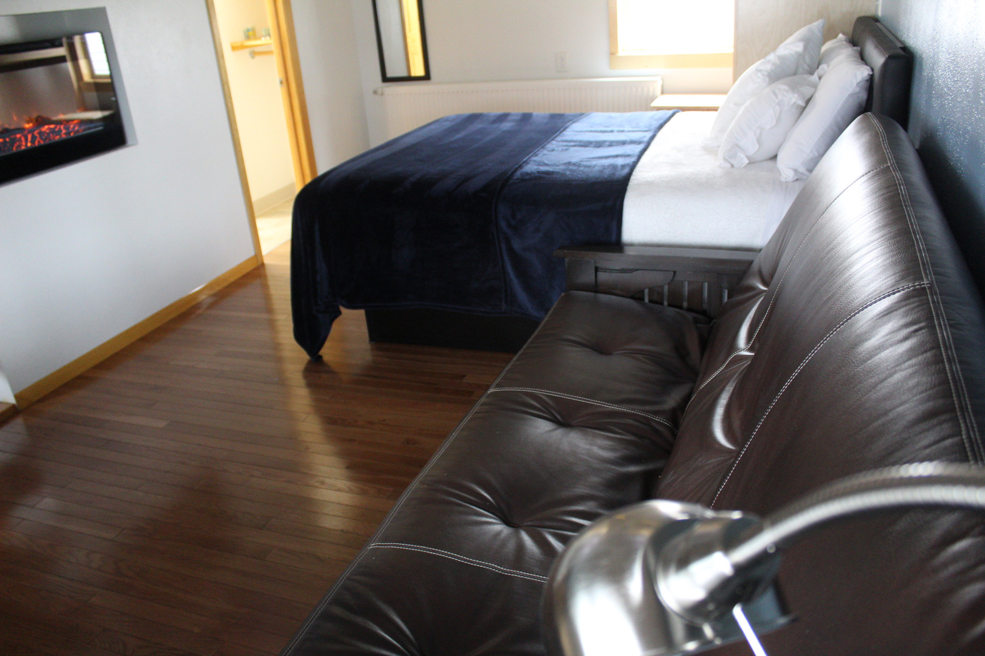 A hotel room with a bed, sofa, TV, and wooden floor.