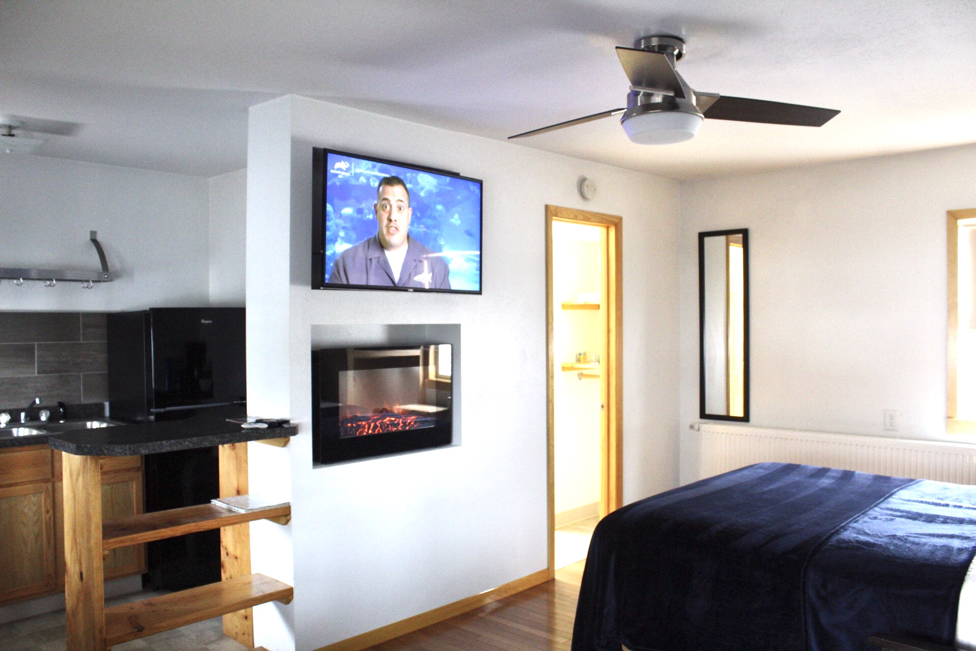 A wide view of a hotel room with a kitchenette, TV, fireplace, and bed.
