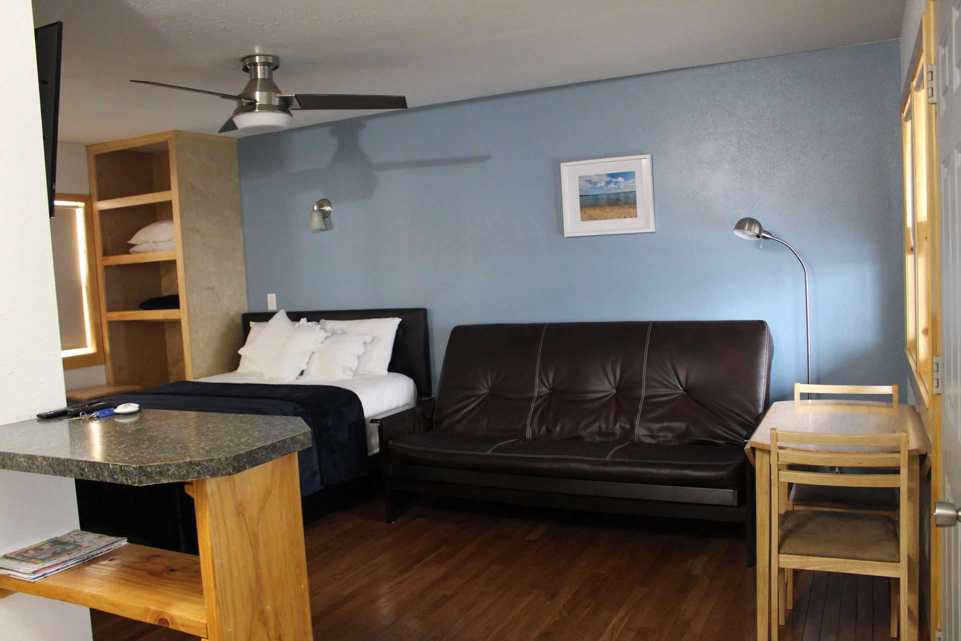 A hotel room with a bed, sofa, desk, and ceiling fan.